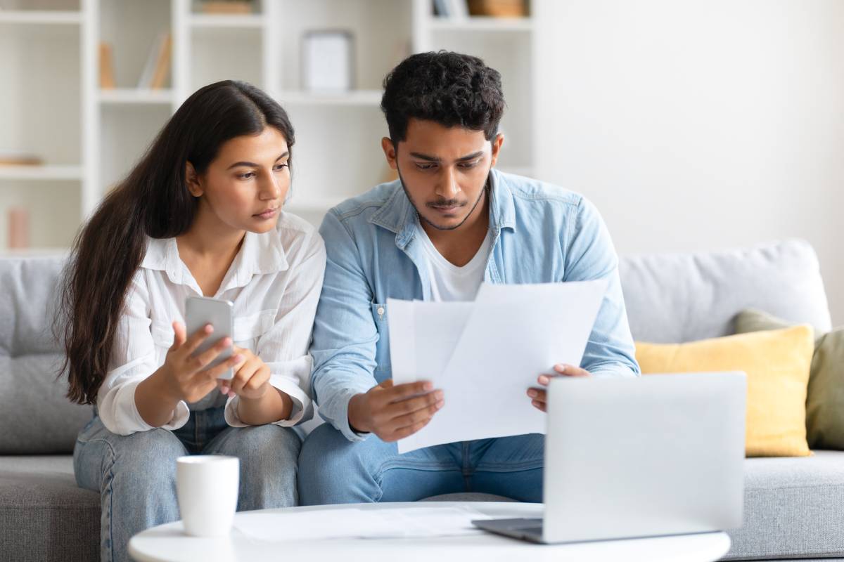indian-couple-focused-bills-using-cellphone-sitting-sofa-1