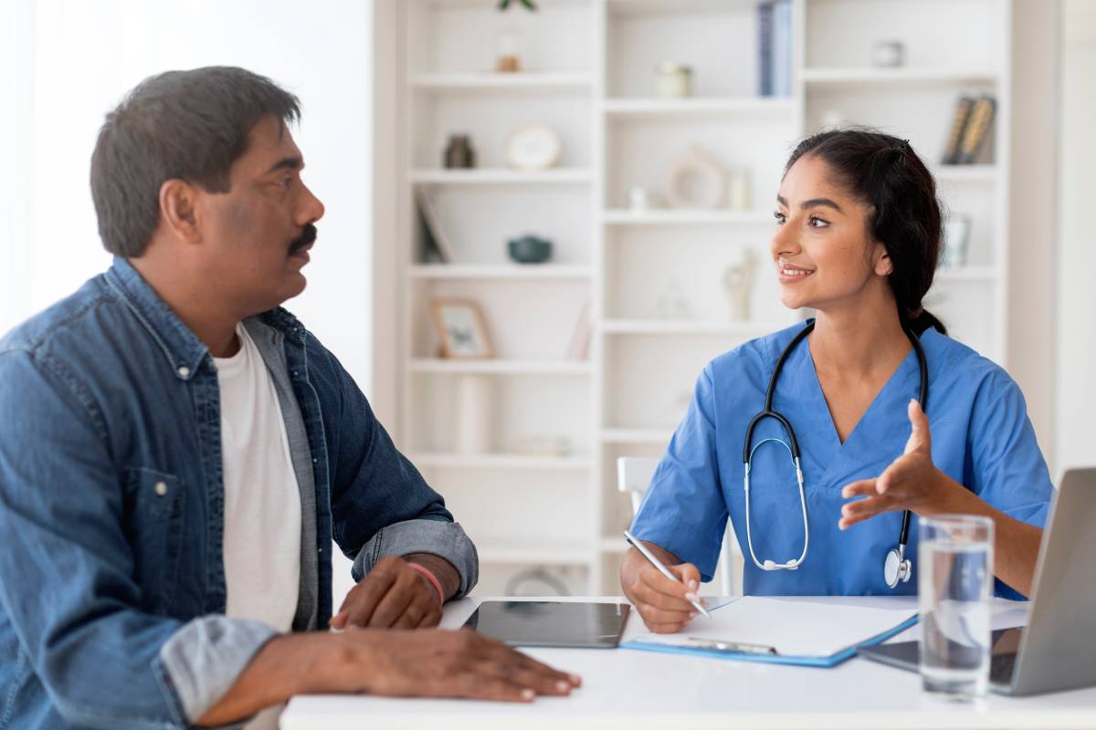 smiling-indian-doctor-woman-talking-male-patient-appointment-office (1)