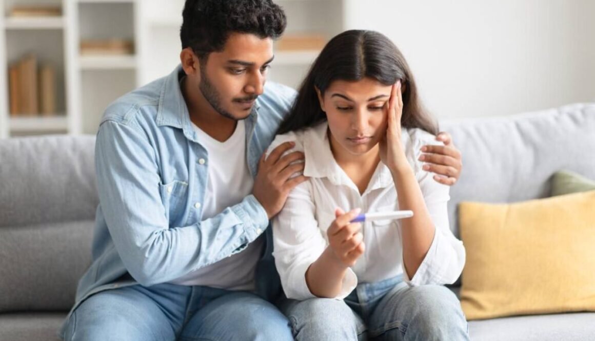unwanted-pregnancy-worried-hindu-couple-looking-positive-test-result-sitting-sofa-home (1)